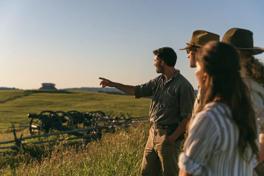 A man points across a grassy field with cannons toward a distant structure.