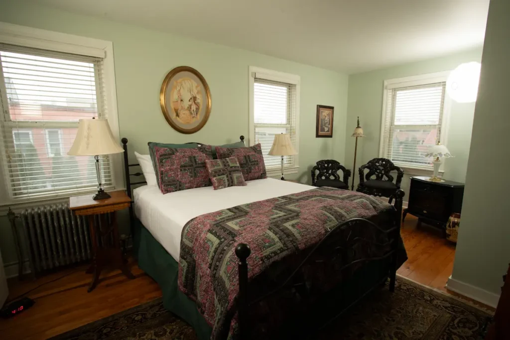 A cozy bedroom with pale green walls, a bed with a patterned quilt, and wooden side tables.