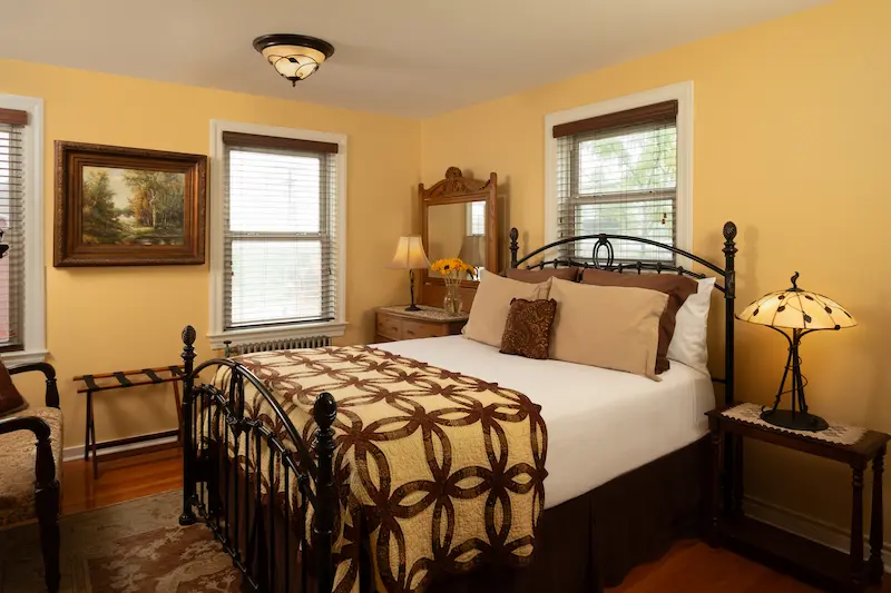 A bedroom with yellow walls, a metal bed frame, patterned bedding, and two windows.
