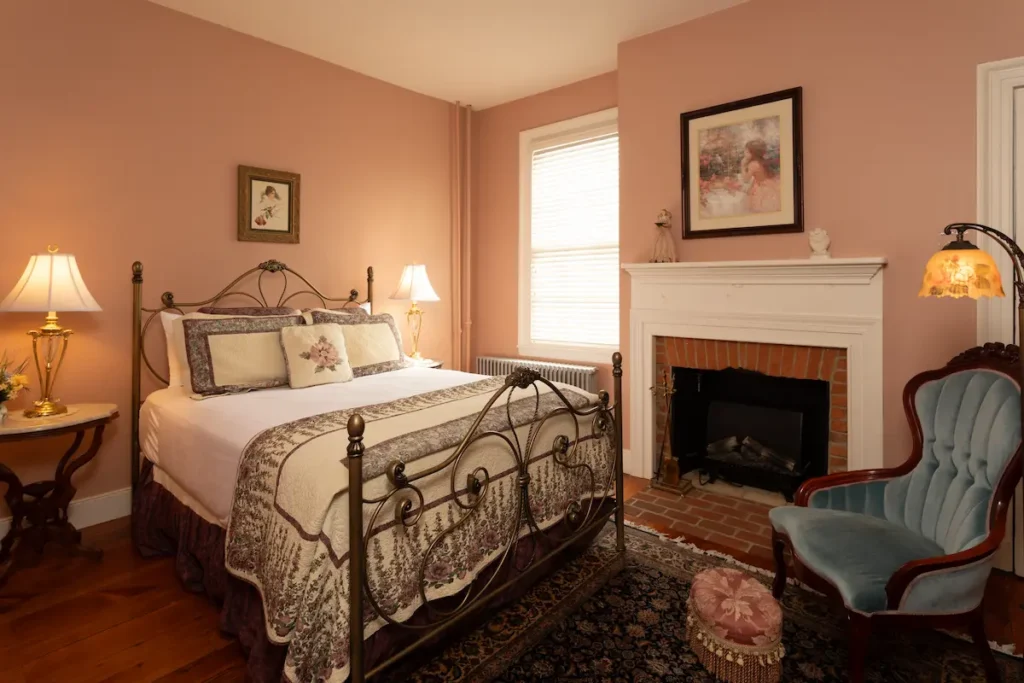 Bedroom with iron bed, fireplace, blue armchair, and pink walls.