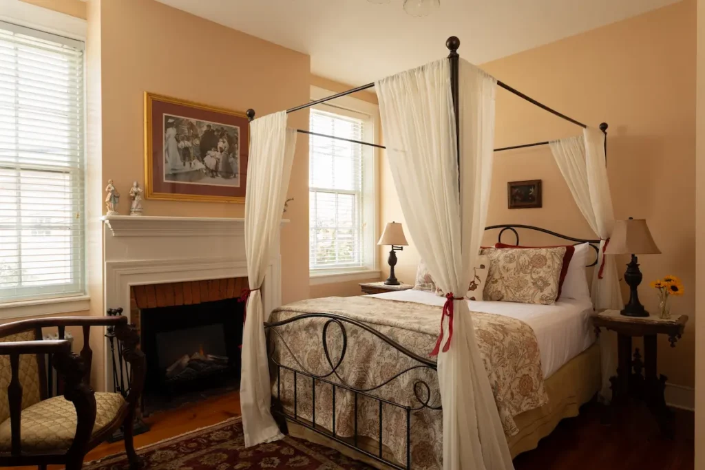 A cozy bedroom with a four-poster canopy bed, fireplace, and peach-colored walls.